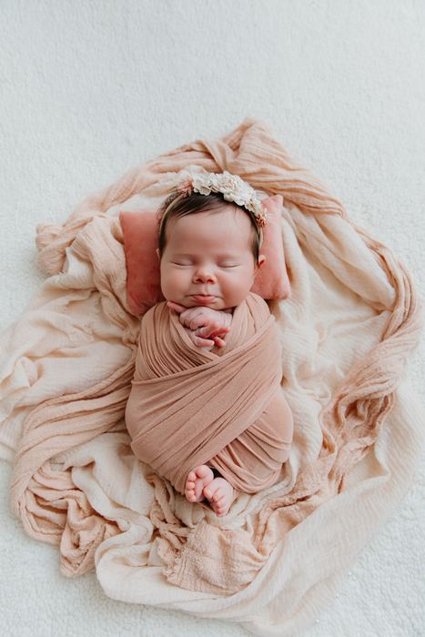 Newborn sleeping, wrapped in a soft blush swaddle