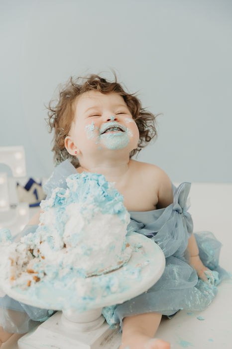 One-year-old laughing, covered in blue and white frosting