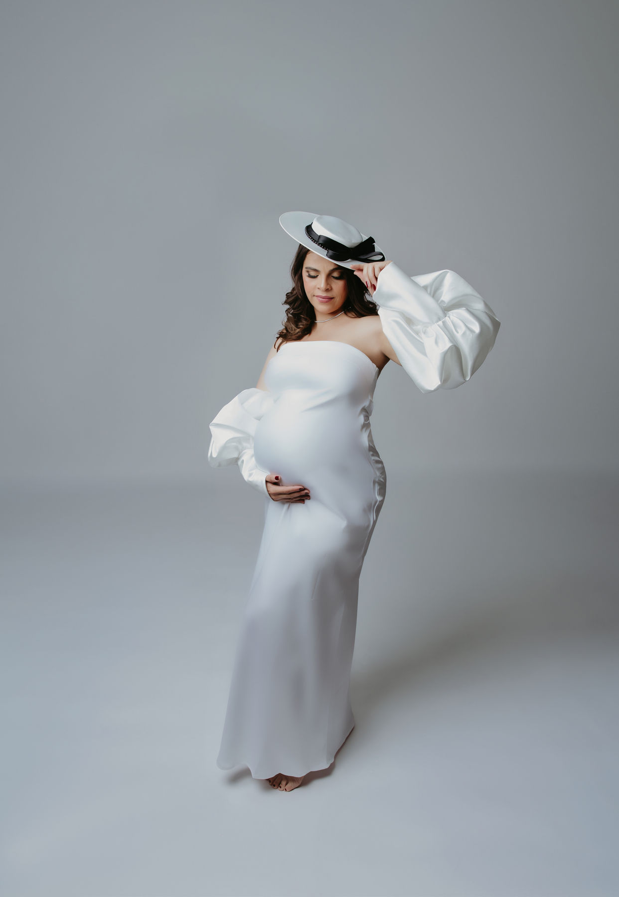 Maternity portrait in a white gown and wide-brim hat