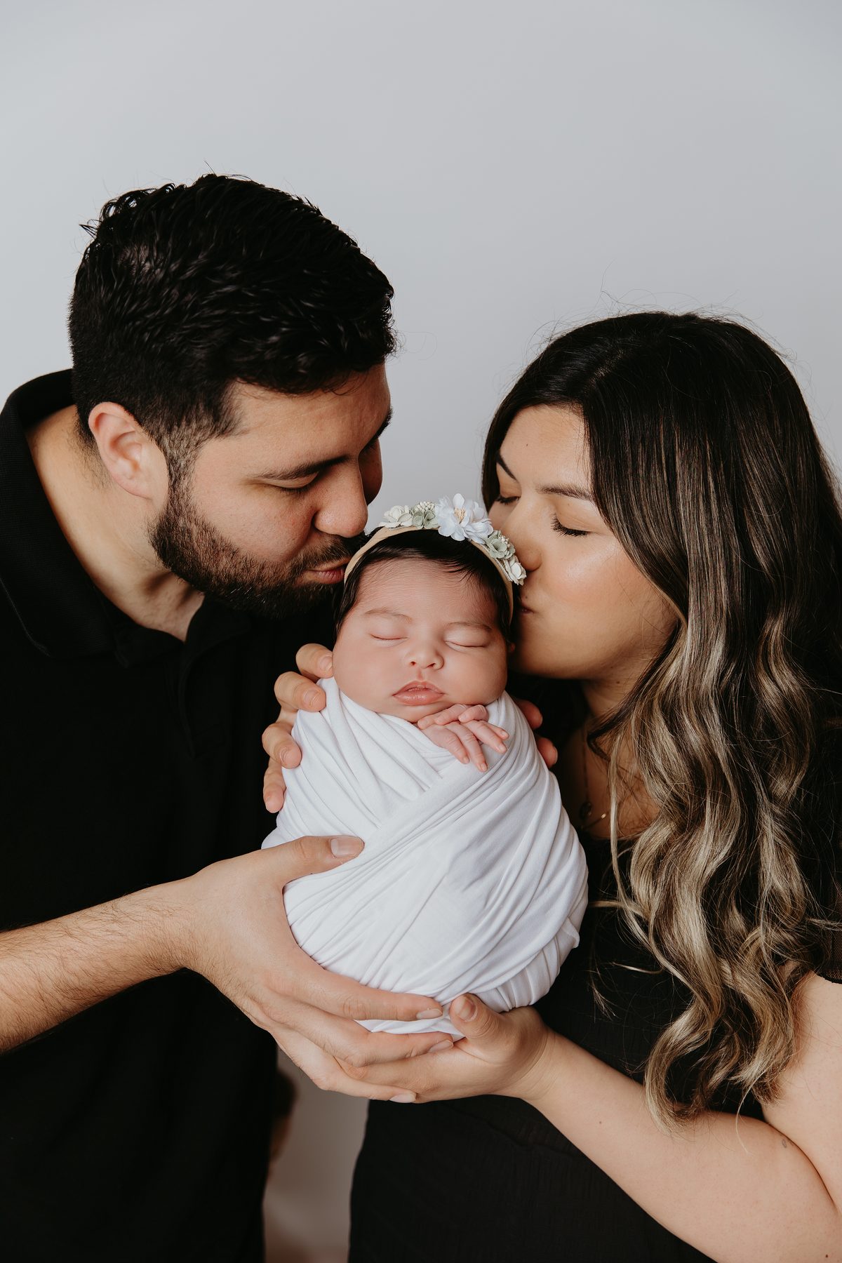 Parents kissing their swaddled newborn daughter